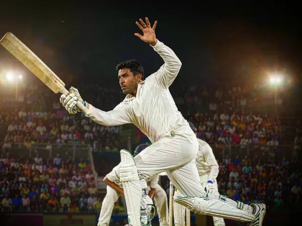 m66 Cricketer in white kit plays a shot under floodlights in a packed night stadium
