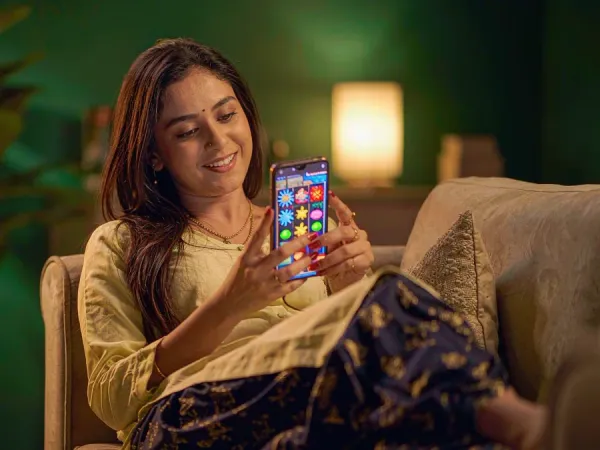 m66 Woman relaxes on a sofa and smiles at a phone showing a colourful slot game