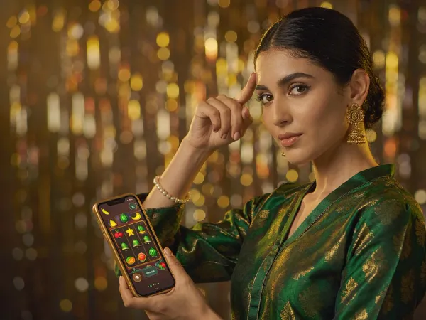 m66 Woman in an emerald and gold kameez holds a phone showing glowing fruit and bell reels