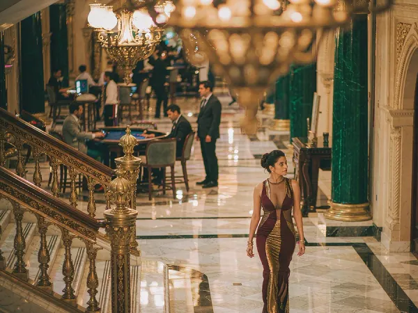 m66 Woman in a maroon and gold dress walks through a chandelier-lit casino lobby