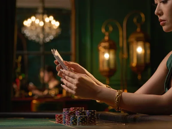 m66 Hands with gold bangles hold three cards beside chip stacks on green felt