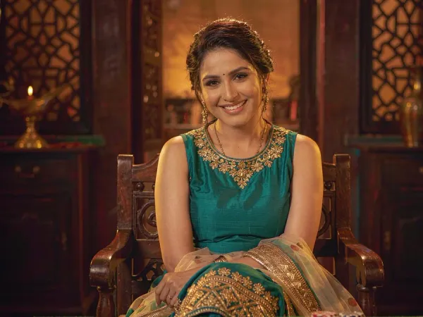 m66 Woman in a teal and gold kameez smiles beside three face-up cards on green felt