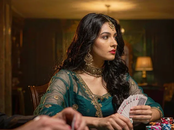 m66 Woman in teal and gold holds cards at a green felt poker table with chips